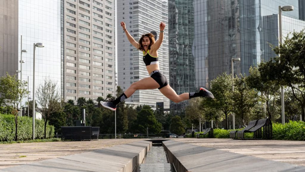 Woman leaping joyfully in an urban park, surrounded by towering skyscrapers.